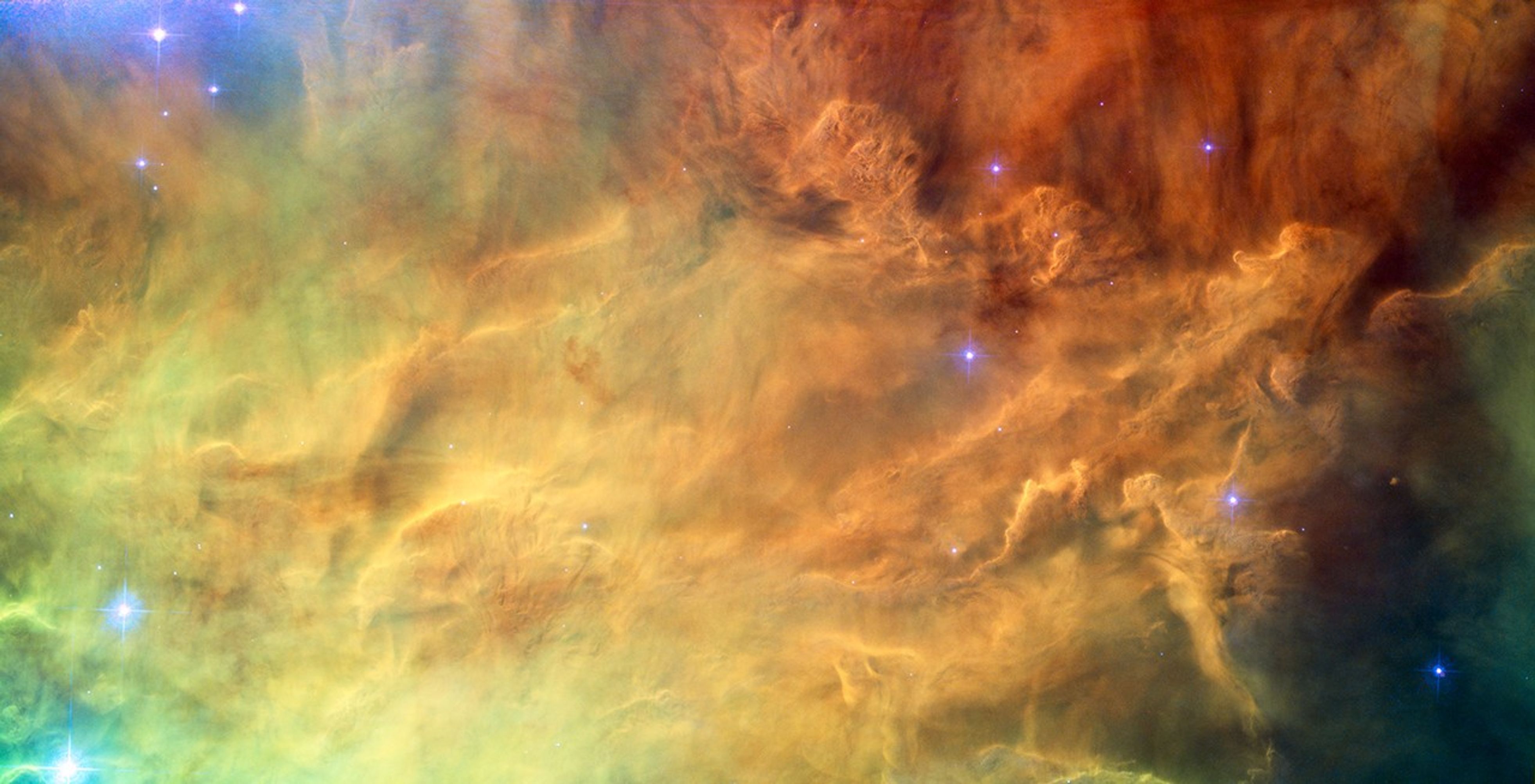 Clouds of gas cover the entire view, in a variety of bold colors. in the center the gas is brighter and very textured, resembling dense smoke. around the edges it is sparser and fainter. several small, bright blue stars are scattered over the nebula.